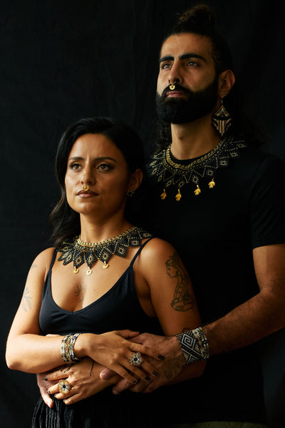 Two people wearing ornate necklaces against a dark background